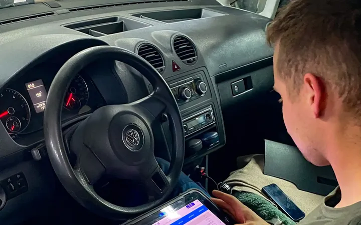 Mechanik odczytuje dane z testera diagnostycznego w kabinie samochodu.