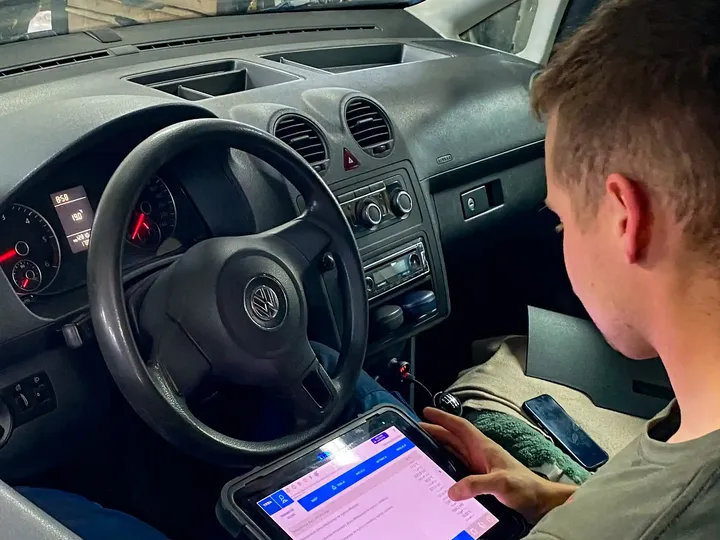 Mechanik odczytuje dane z testera diagnostycznego w kabinie samochodu.