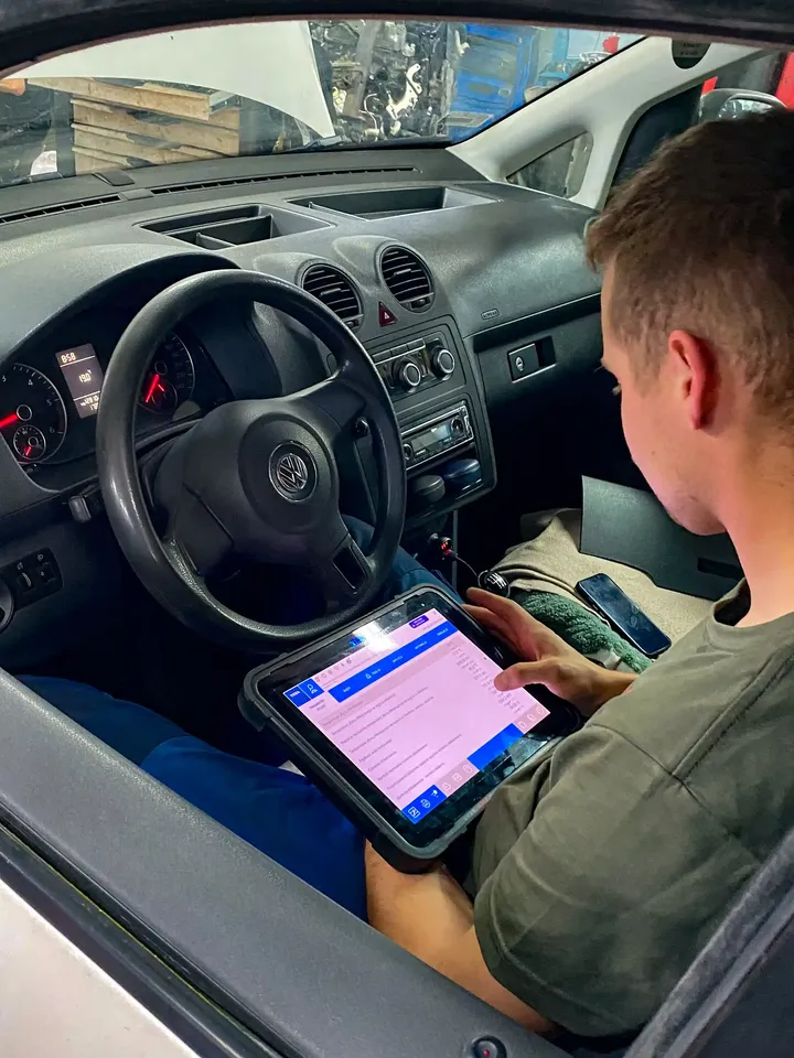 Mechanik odczytuje dane z testera diagnostycznego w kabinie samochodu.