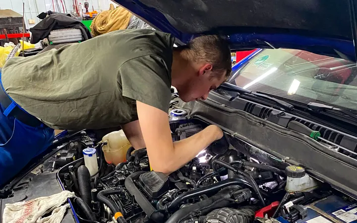 Mechanik pracuje pod otwartą maską samochodu.