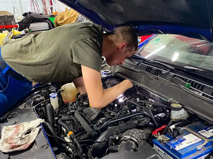 Mechanik pracuje pod otwartą maską samochodu.