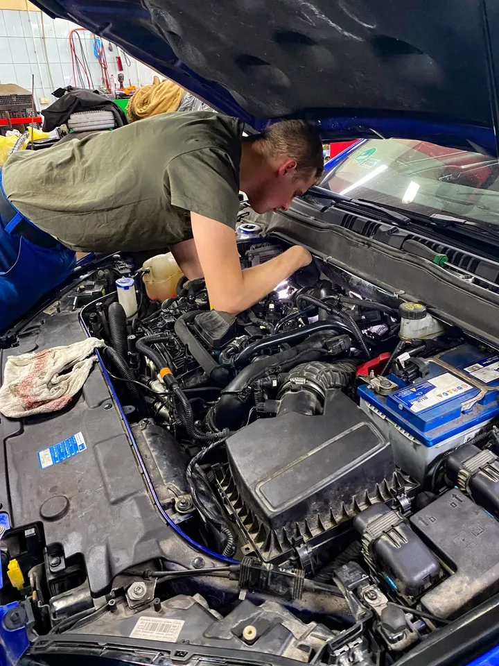 Mechanik pracuje pod otwartą maską samochodu.
