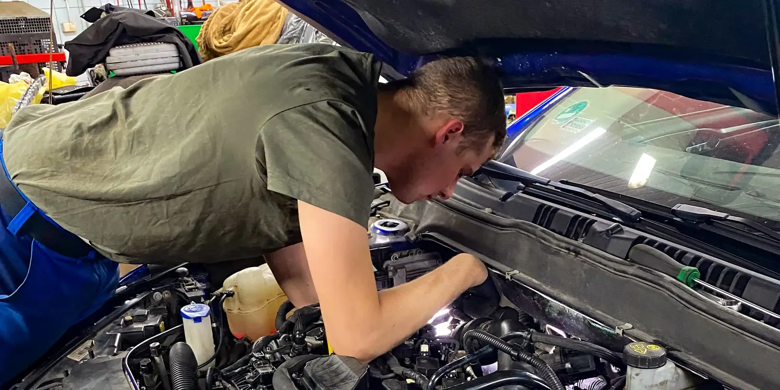 Mechanik pracuje pod otwartą maską samochodu.
