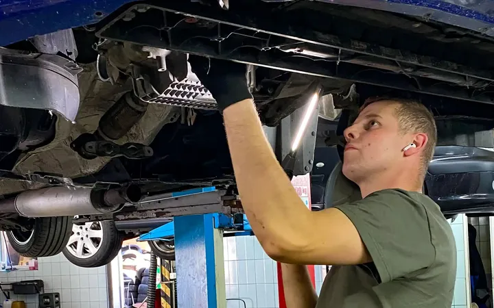 Mechanik pracuje pod niebieskim samochodem na podnośniku.