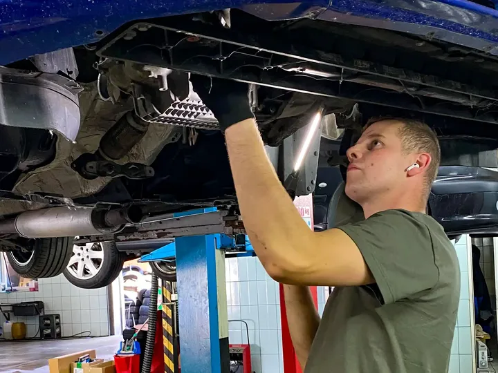 Mechanik pracuje pod niebieskim samochodem na podnośniku.