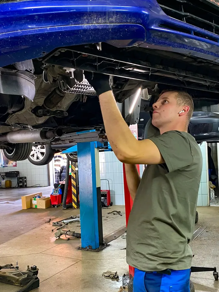 Mechanik pracuje pod niebieskim samochodem na podnośniku.