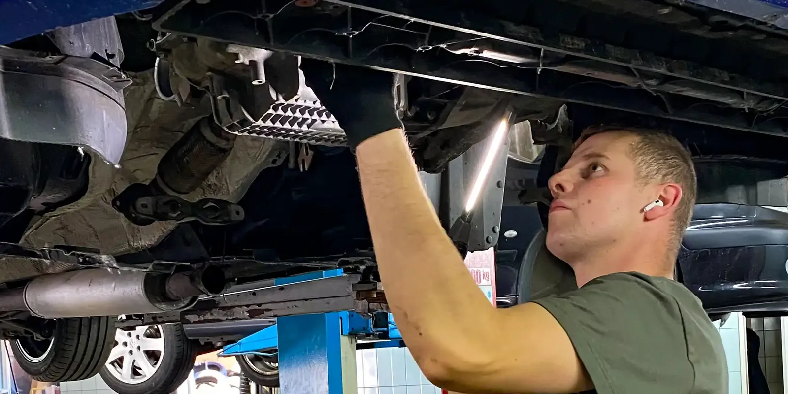 Mechanik pracuje pod niebieskim samochodem na podnośniku.