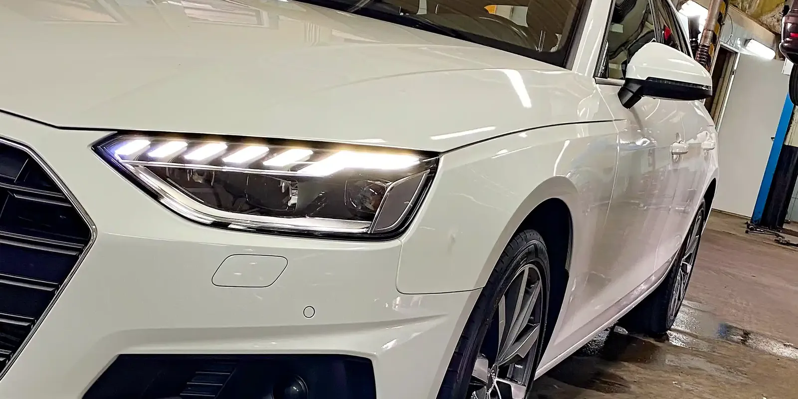 Białe Audi na stanowisku warsztatowym z przodu.