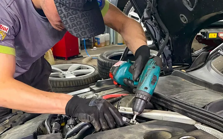 Mechanik z narzędziem pracuje przy komorze silnika osłoniętej matą ochronną.