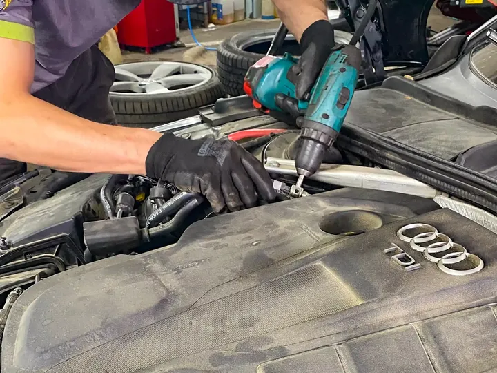 Mechanik z narzędziem pracuje przy komorze silnika osłoniętej matą ochronną.