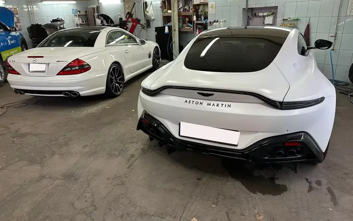 Białe samochody, w tym Aston Martin, we wnętrzu warsztatu.