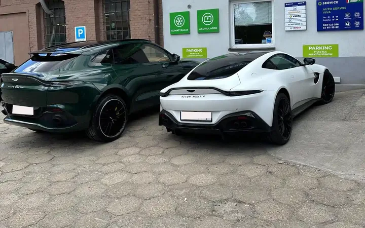 Biały Aston Martin i zielony SUV Aston Martin przed budynkiem Auto Serwis VIVA.