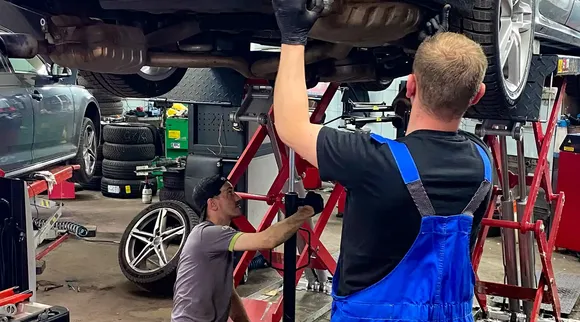 Dwóch mechaników pracuje przy Audi uniesionym na podnośniku.