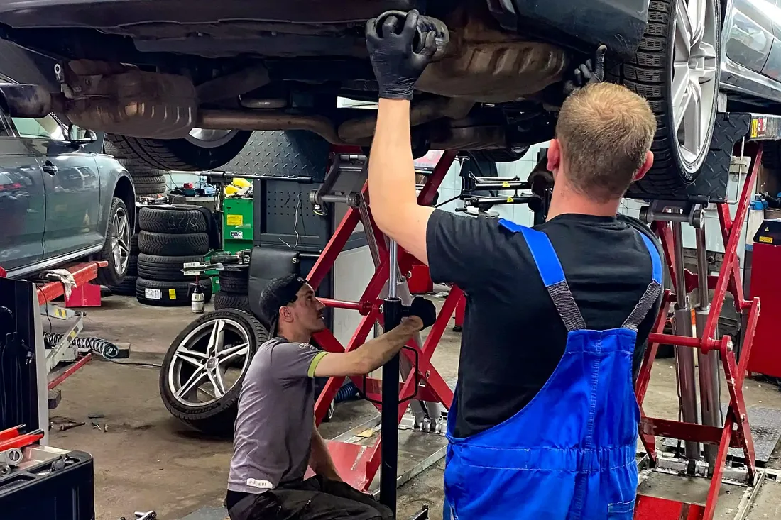 Dwóch mechaników pracuje przy Audi uniesionym na podnośniku.