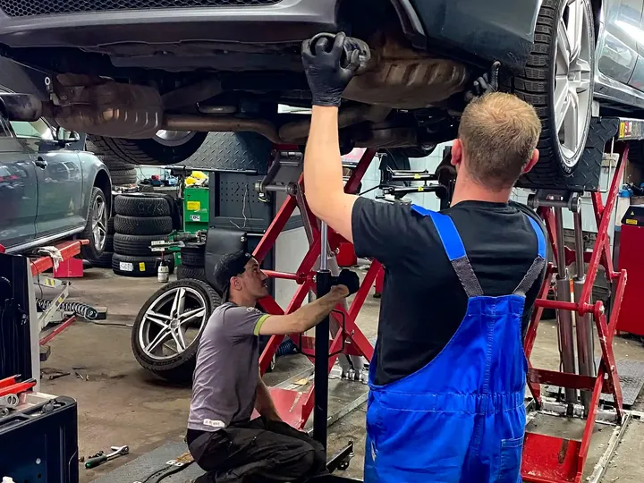 Dwóch mechaników pracuje przy Audi uniesionym na podnośniku.