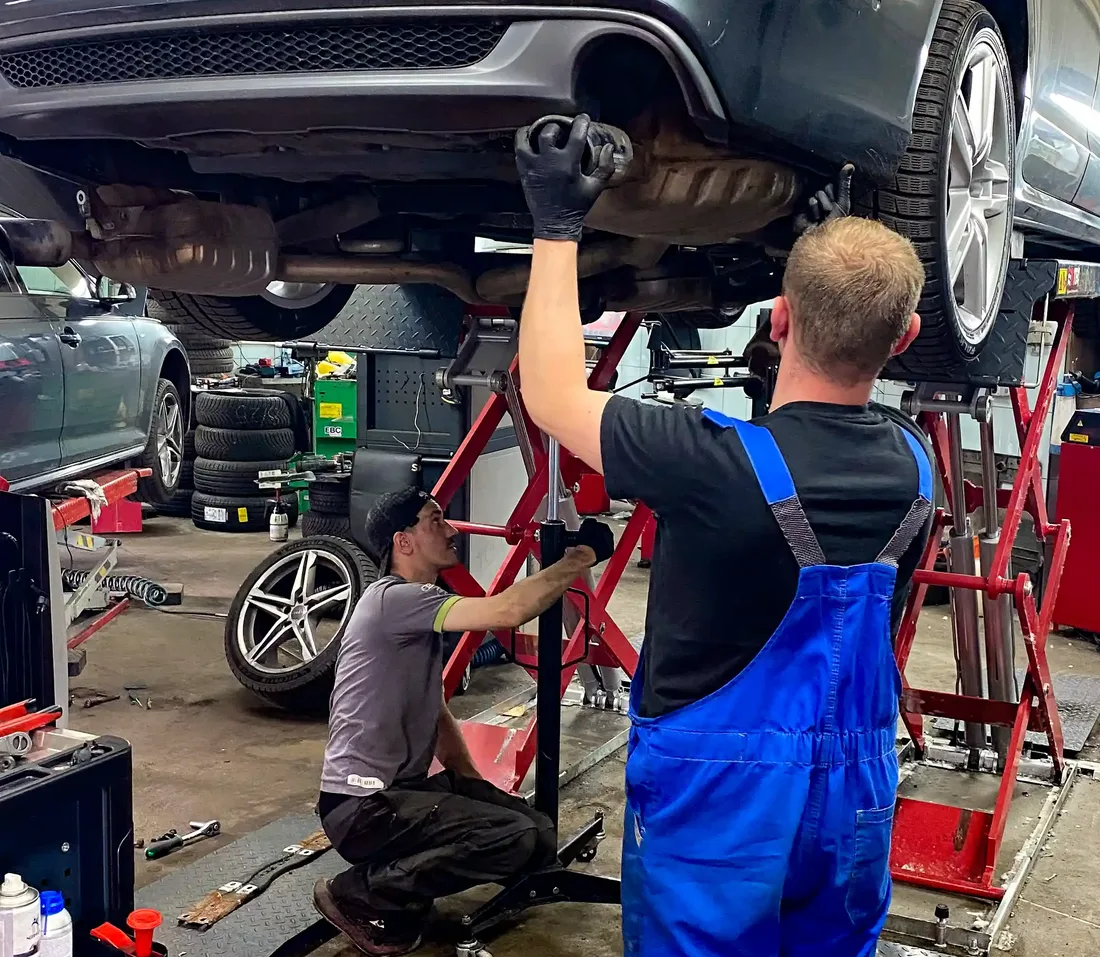 Dwóch mechaników pracuje przy Audi uniesionym na podnośniku.
