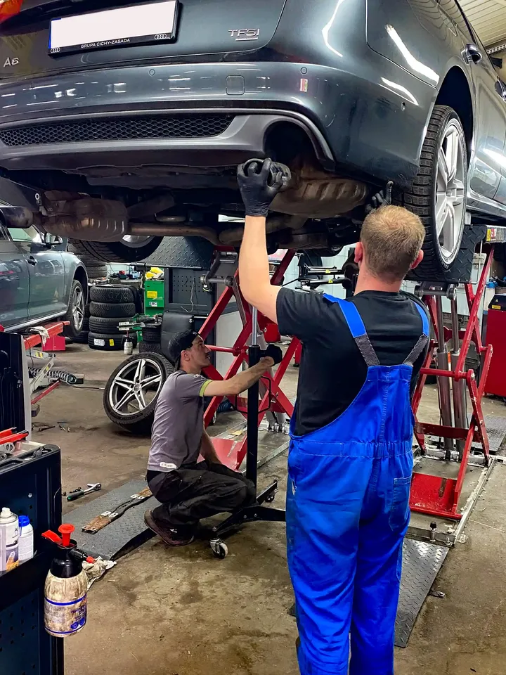 Dwóch mechaników pracuje przy Audi uniesionym na podnośniku.