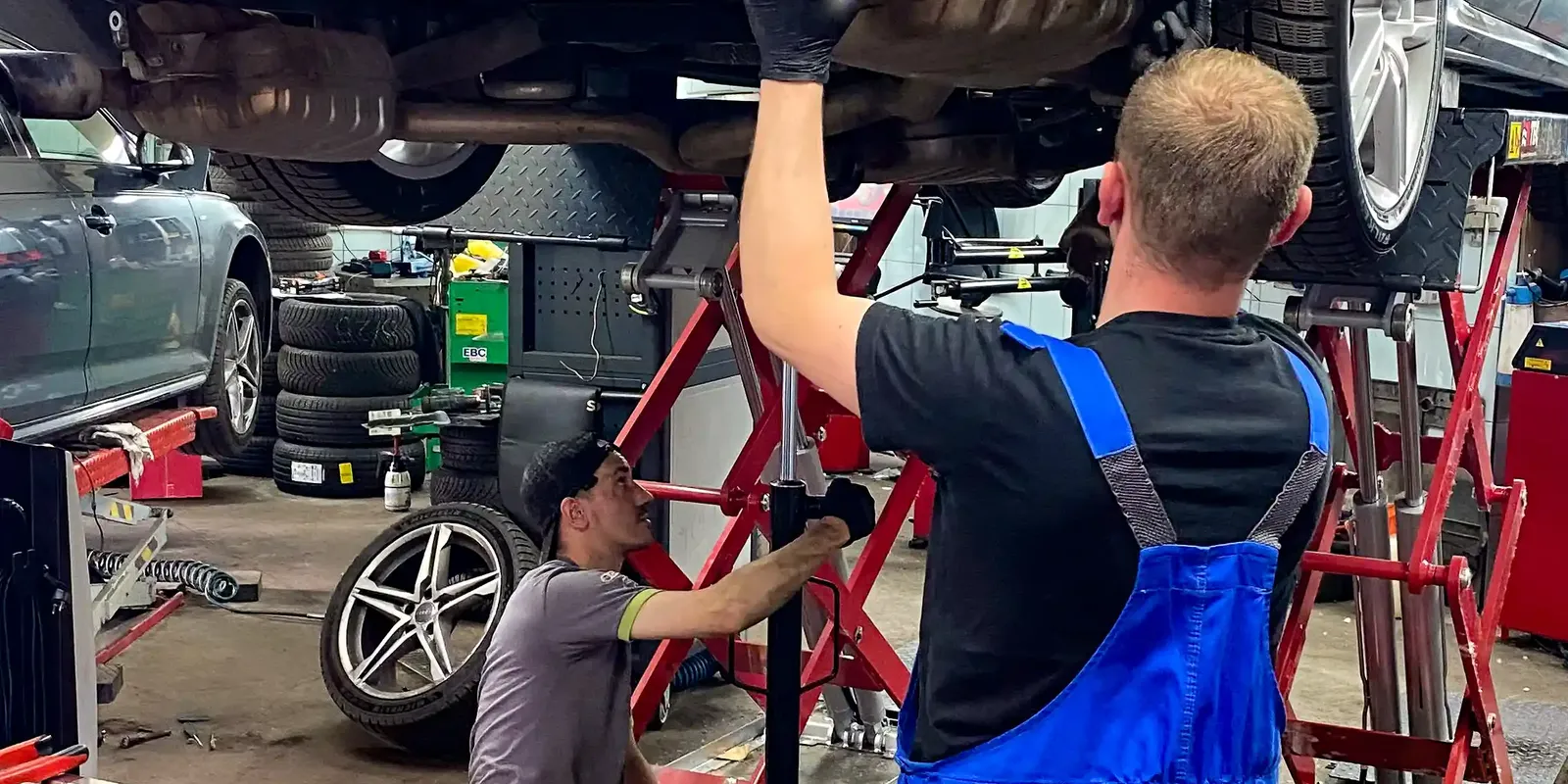 Dwóch mechaników pracuje przy Audi uniesionym na podnośniku.