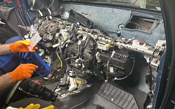 Mechanik pracuje przy rozebranej desce rozdzielczej i układzie ogrzewania.