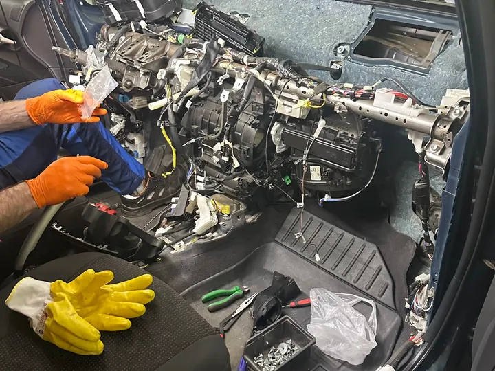 Mechanik pracuje przy rozebranej desce rozdzielczej i układzie ogrzewania.