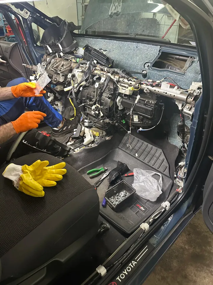 Mechanik pracuje przy rozebranej desce rozdzielczej i układzie ogrzewania.