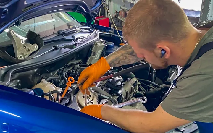 Mechanik pracuje przy odsłoniętym rozrządzie niebieskiego samochodu.