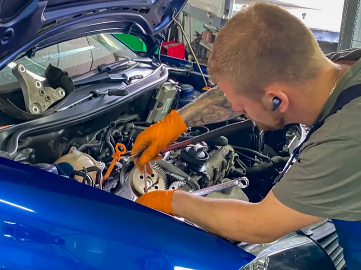 Mechanik pracuje przy odsłoniętym rozrządzie niebieskiego samochodu.