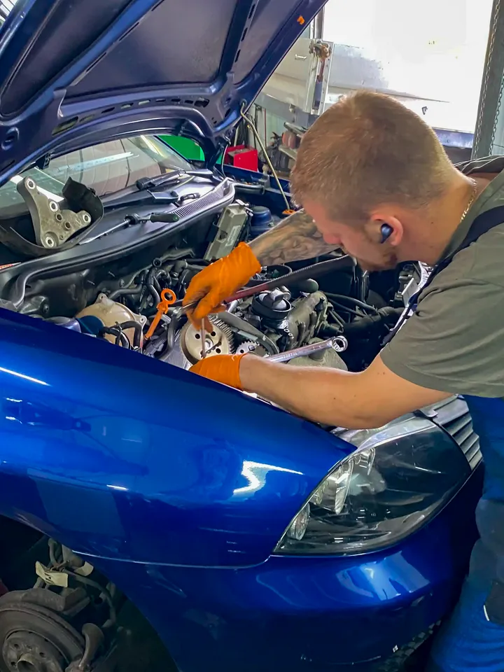Mechanik pracuje przy odsłoniętym rozrządzie niebieskiego samochodu.