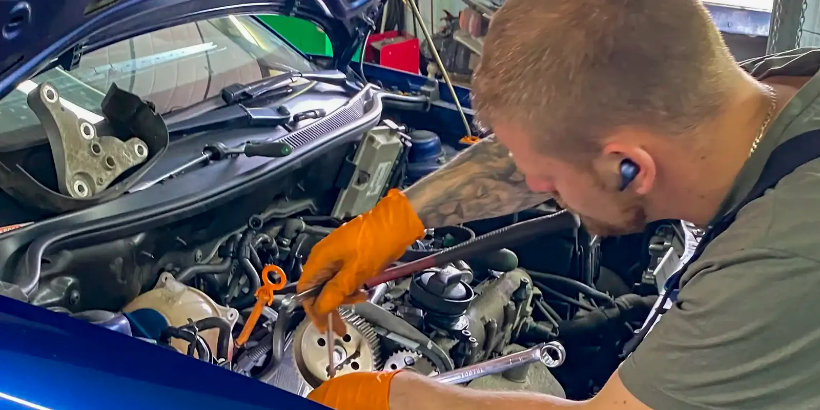 Mechanik pracuje przy odsłoniętym rozrządzie niebieskiego samochodu.